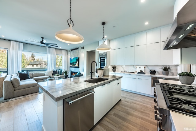 kitchen featuring stainless steel dishwasher, wall chimney exhaust hood, sink, white cabinets, and hanging light fixtures