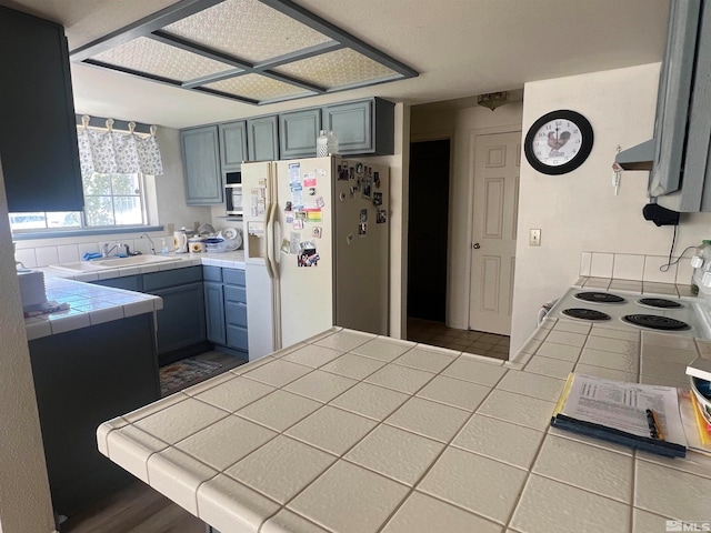 kitchen featuring gray cabinets, white appliances, sink, and tile counters