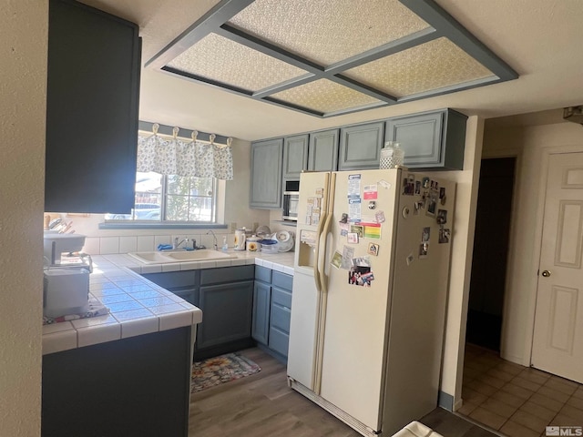 kitchen featuring gray cabinetry, dark hardwood / wood-style floors, tile countertops, sink, and white fridge with ice dispenser