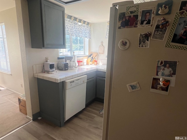 kitchen with gray cabinetry, light hardwood / wood-style flooring, white dishwasher, and tile counters