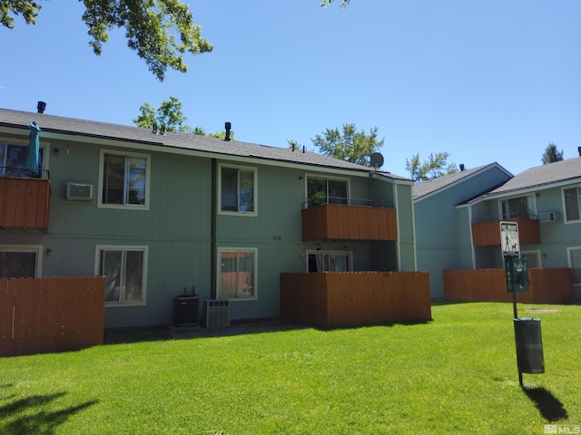 rear view of house with a balcony, a lawn, a wall unit AC, and cooling unit