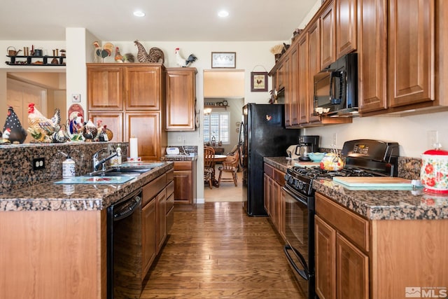 kitchen with a sink, dark wood-style floors, black appliances, brown cabinetry, and dark countertops