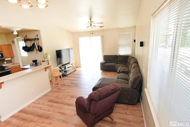 living room featuring ceiling fan with notable chandelier and light hardwood / wood-style flooring