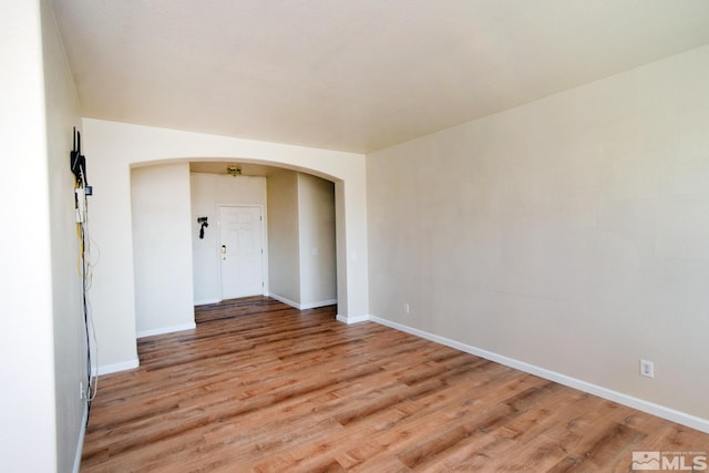 unfurnished room with light wood-style floors, arched walkways, and baseboards