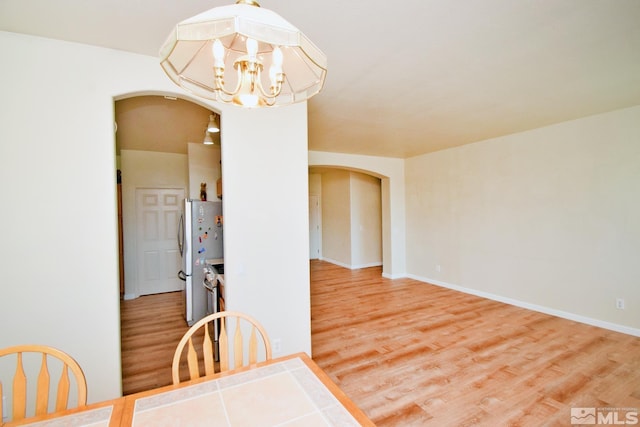 dining room featuring an inviting chandelier, baseboards, arched walkways, and wood finished floors