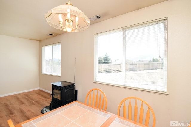 dining room with a notable chandelier, visible vents, a wood stove, wood finished floors, and baseboards