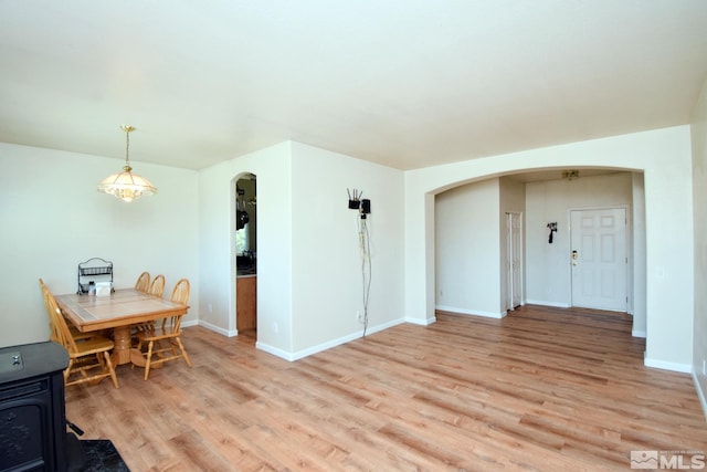 dining room featuring arched walkways, light wood-type flooring, a wood stove, and baseboards