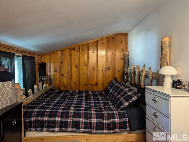 bedroom featuring lofted ceiling and wooden walls