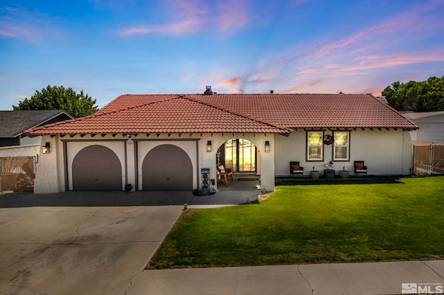 mediterranean / spanish home with driveway, an attached garage, fence, a yard, and stucco siding