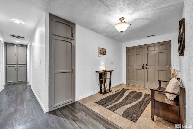 entrance foyer with visible vents, a textured wall, a textured ceiling, and wood finished floors