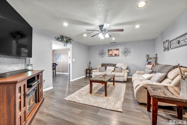 living area featuring ceiling fan, a textured ceiling, baseboards, and wood finished floors