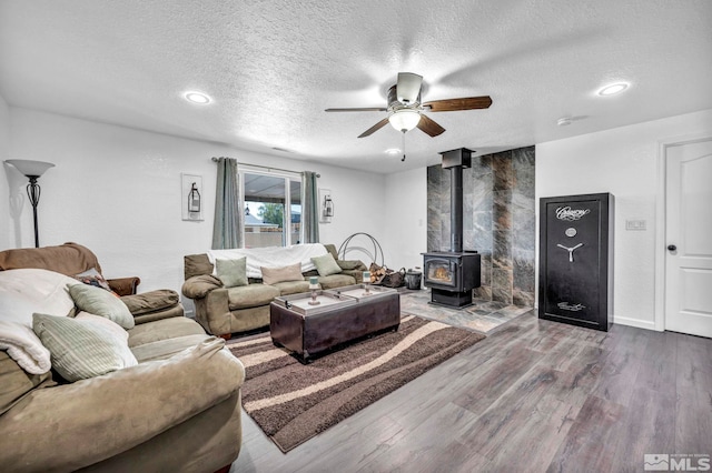 living room with baseboards, ceiling fan, wood finished floors, a wood stove, and a textured ceiling