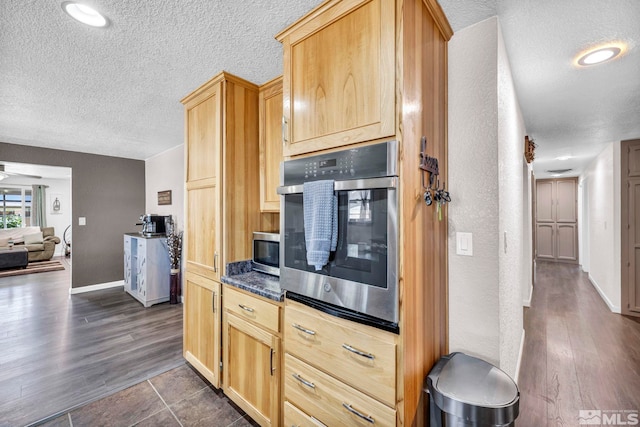 kitchen featuring a textured ceiling, baseboards, appliances with stainless steel finishes, dark countertops, and dark wood finished floors