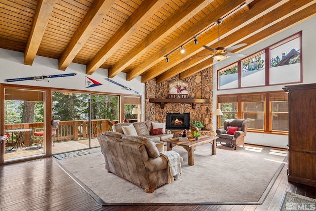 living room with ceiling fan, a stone fireplace, wooden ceiling, hardwood / wood-style flooring, and beam ceiling