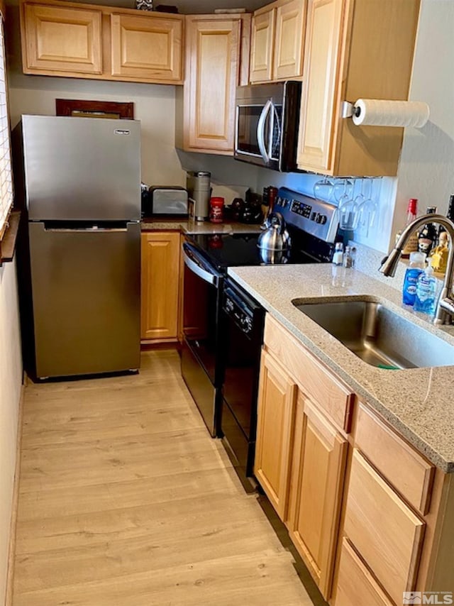 kitchen with light stone counters, light brown cabinets, a sink, light wood-style floors, and appliances with stainless steel finishes