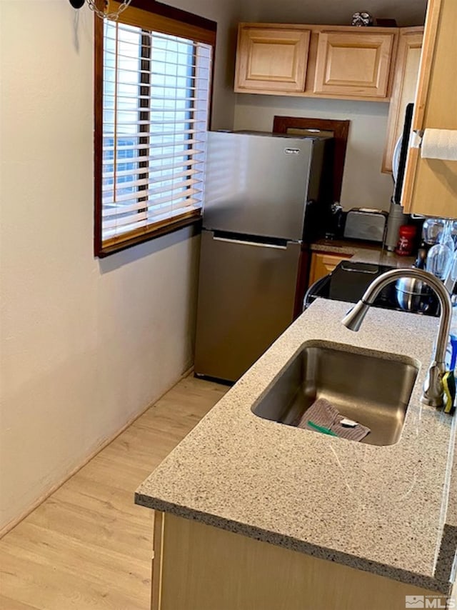 kitchen with light stone counters, a sink, freestanding refrigerator, light brown cabinetry, and light wood finished floors