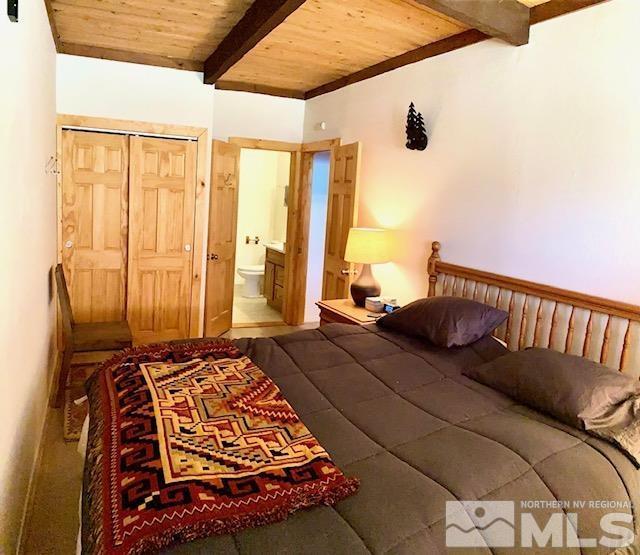 bedroom featuring wooden ceiling, ensuite bath, and beam ceiling