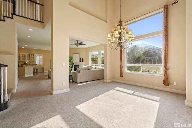 dining area featuring ceiling fan with notable chandelier, light carpet, and a towering ceiling