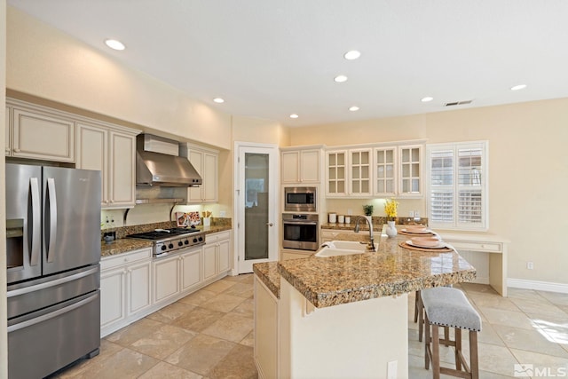 kitchen featuring appliances with stainless steel finishes, light stone countertops, sink, wall chimney exhaust hood, and a kitchen breakfast bar