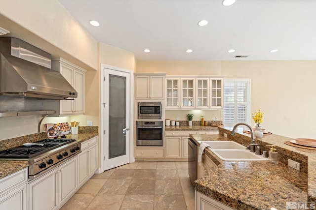 kitchen with appliances with stainless steel finishes, stone counters, and wall chimney range hood