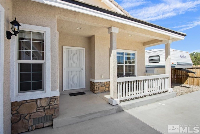 property entrance featuring stone siding, fence, covered porch, and stucco siding