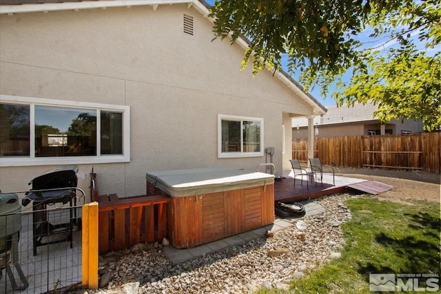 rear view of house featuring stucco siding, fence, a wooden deck, and a hot tub