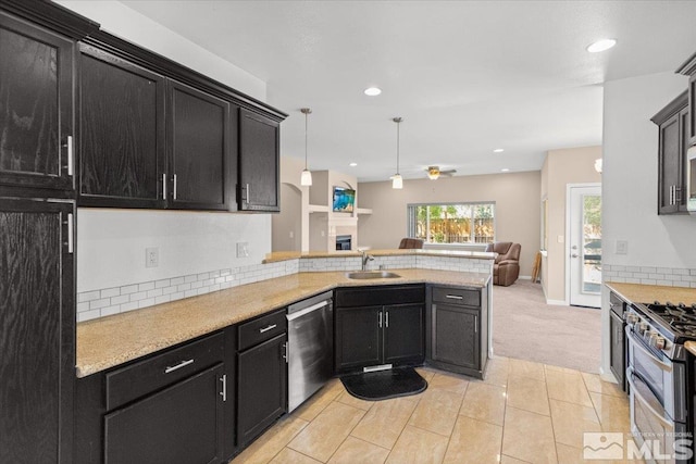 kitchen featuring open floor plan, a peninsula, stainless steel appliances, dark cabinetry, and a sink