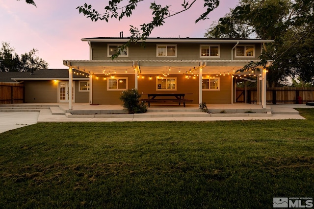 back house at dusk featuring a yard and a patio area