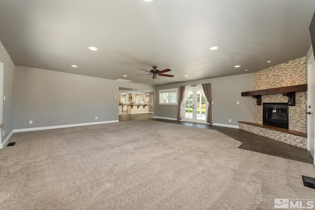 unfurnished living room with a large fireplace, ceiling fan, and dark colored carpet