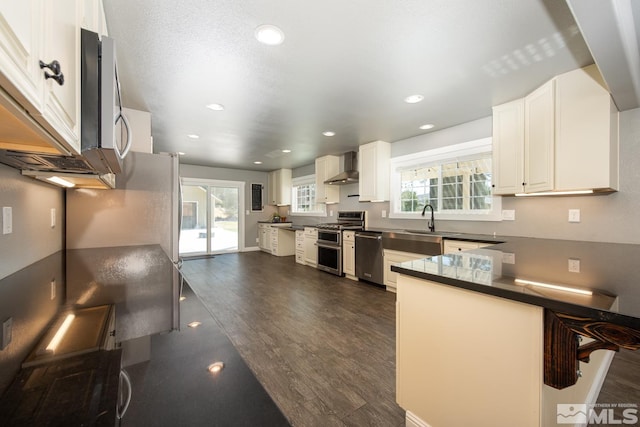 kitchen with dark hardwood / wood-style floors, appliances with stainless steel finishes, white cabinetry, plenty of natural light, and wall chimney range hood