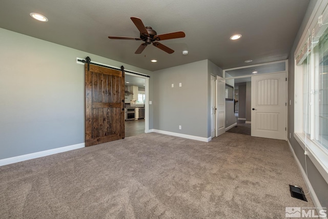 interior space with ceiling fan, a barn door, and carpet floors