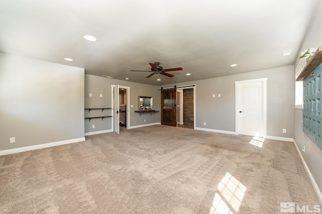 unfurnished living room featuring light colored carpet, ceiling fan, and a barn door