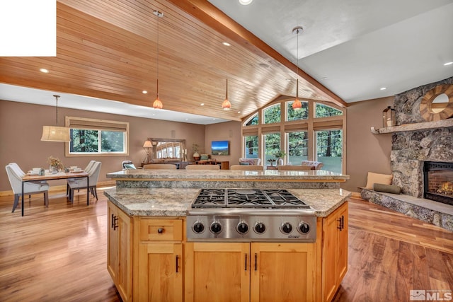 kitchen with light hardwood / wood-style floors, stainless steel gas cooktop, a stone fireplace, pendant lighting, and vaulted ceiling with beams