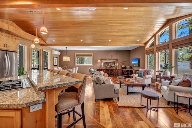 living room featuring plenty of natural light, vaulted ceiling, light wood-type flooring, and a wall mounted air conditioner