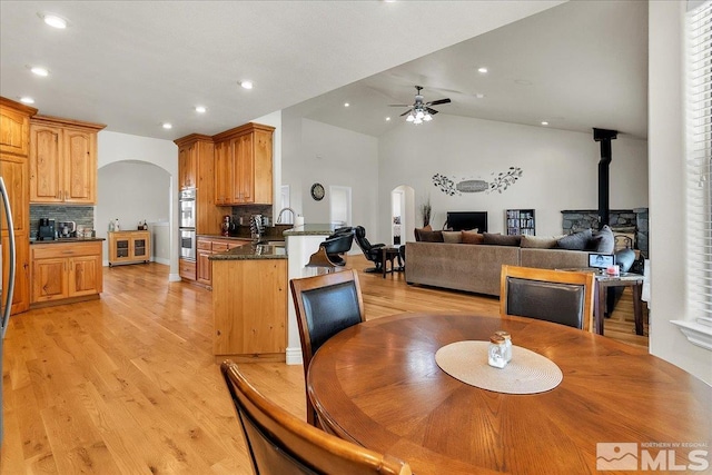 dining room featuring a wood stove, light hardwood / wood-style floors, lofted ceiling, plenty of natural light, and ceiling fan