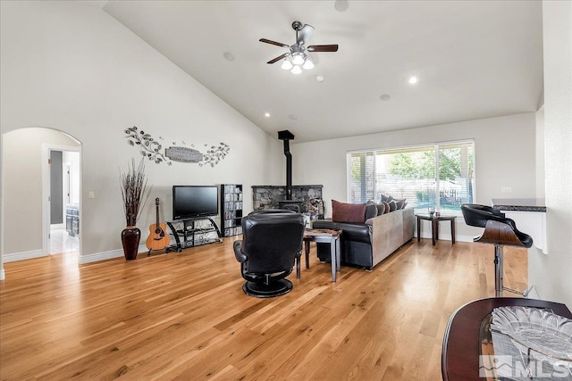 living room with high vaulted ceiling, ceiling fan, a wood stove, and light hardwood / wood-style flooring