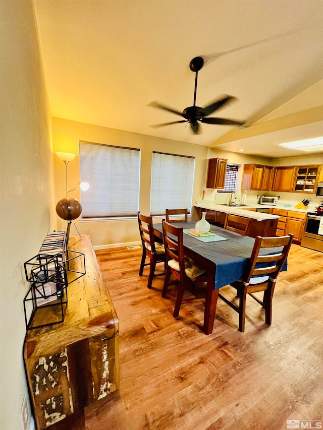 dining space featuring sink, ceiling fan, light hardwood / wood-style floors, and vaulted ceiling