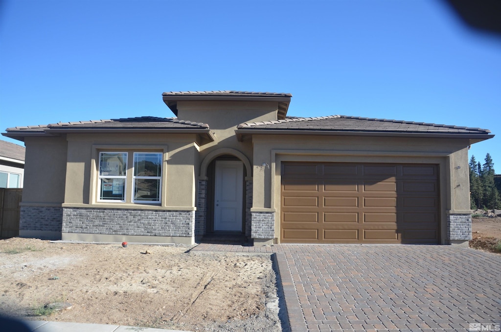 prairie-style house with a garage, brick siding, a tiled roof, decorative driveway, and stucco siding