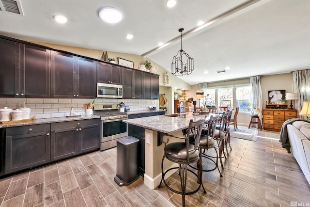 kitchen featuring light hardwood / wood-style flooring, decorative light fixtures, vaulted ceiling, light stone countertops, and stainless steel appliances