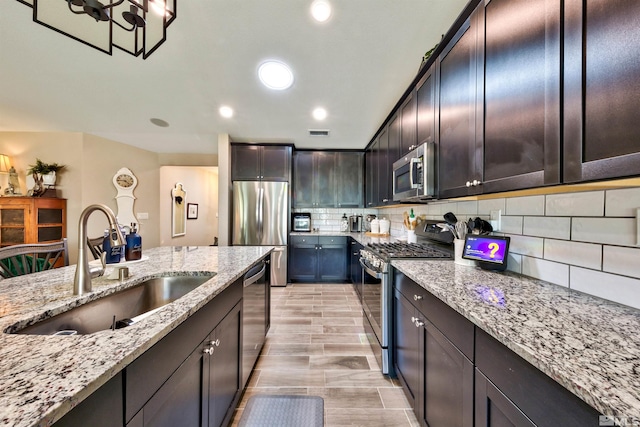 kitchen with light stone counters, stainless steel appliances, sink, dark brown cabinets, and decorative backsplash