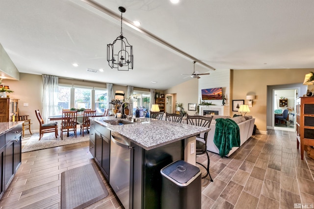 kitchen with ceiling fan with notable chandelier, dishwasher, sink, light stone countertops, and vaulted ceiling