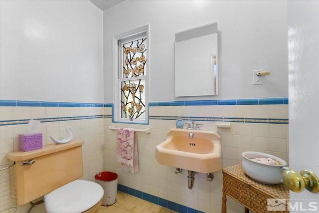 bathroom featuring toilet, tile patterned flooring, sink, decorative backsplash, and tile walls