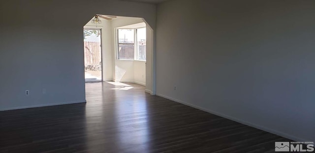 empty room featuring dark wood-type flooring, arched walkways, ceiling fan, and baseboards