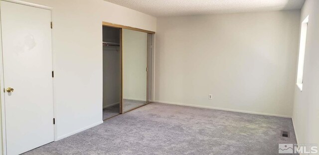 unfurnished bedroom featuring a textured ceiling, a closet, and light carpet