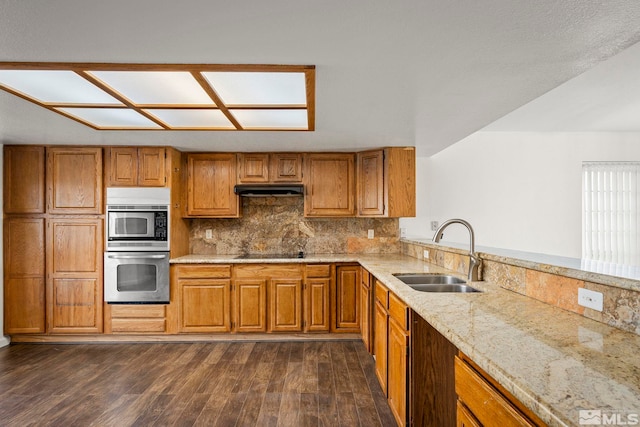 kitchen featuring appliances with stainless steel finishes, brown cabinetry, a sink, and dark wood-style floors