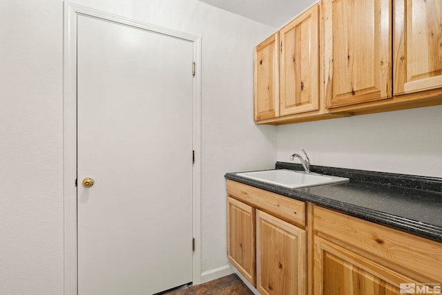 kitchen with light brown cabinets, dark countertops, a sink, and baseboards