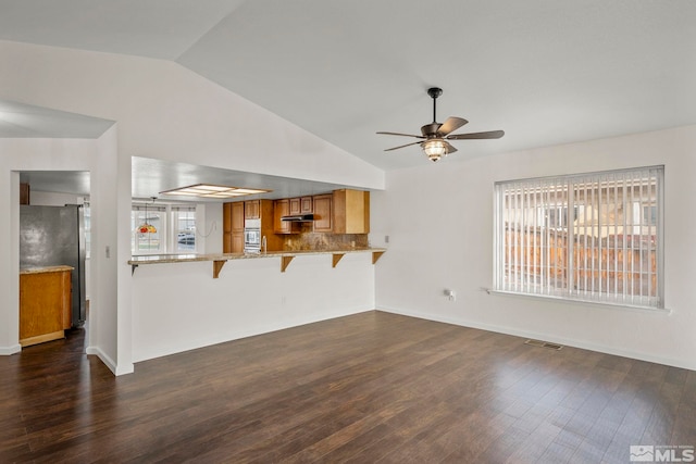 unfurnished living room with baseboards, visible vents, ceiling fan, dark wood-style flooring, and vaulted ceiling