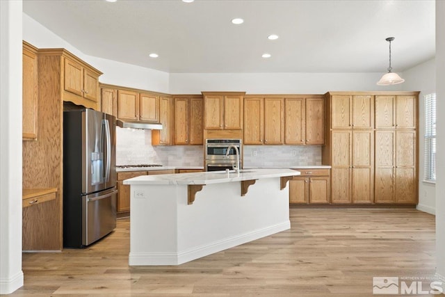 kitchen featuring backsplash, light hardwood / wood-style flooring, appliances with stainless steel finishes, an island with sink, and a kitchen bar