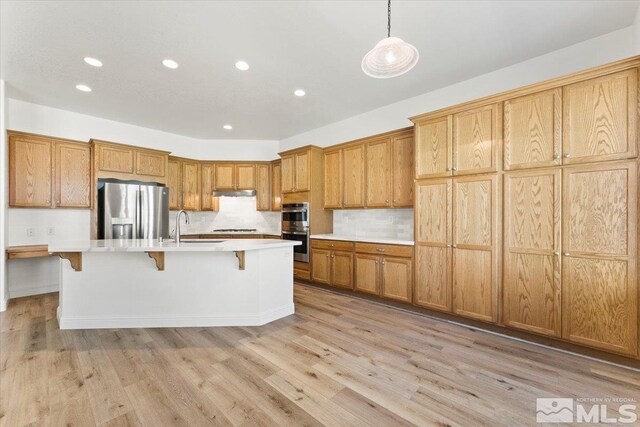 kitchen featuring light hardwood / wood-style flooring, a kitchen island with sink, a kitchen bar, hanging light fixtures, and stainless steel appliances