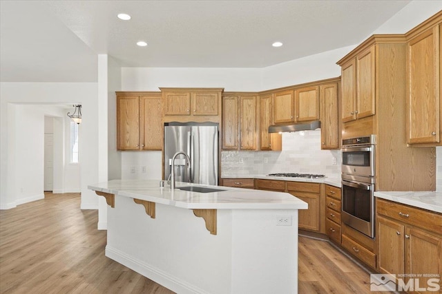 kitchen featuring a kitchen breakfast bar, a center island with sink, appliances with stainless steel finishes, light hardwood / wood-style floors, and sink